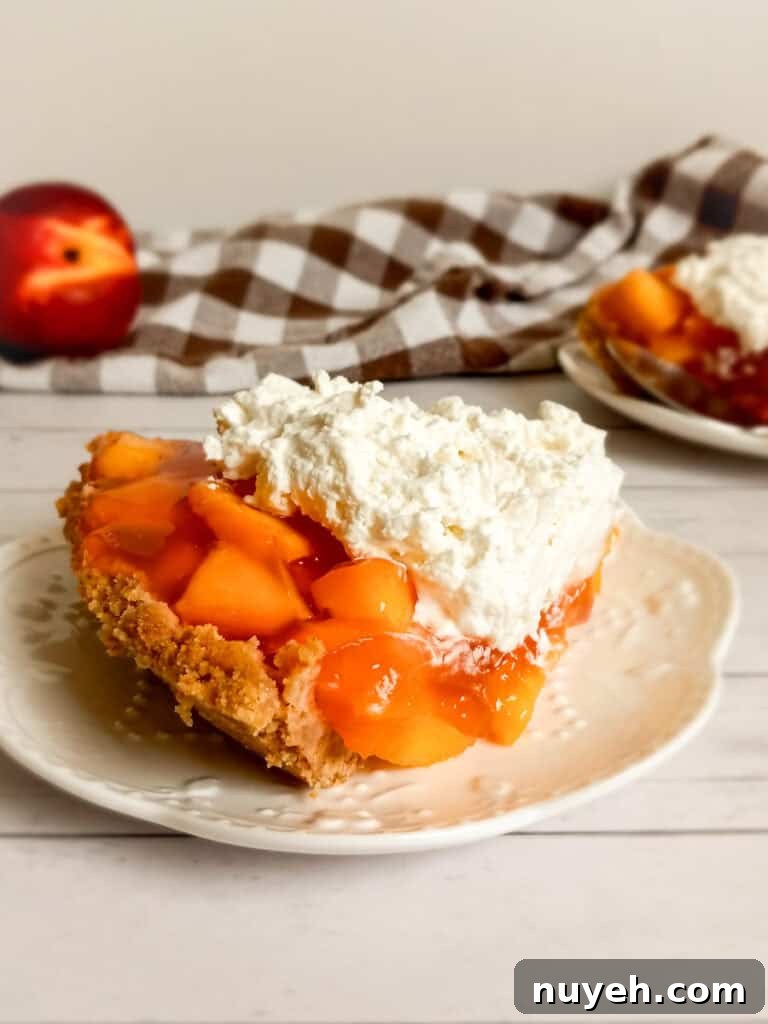 a full-sized photo of a slice of peach pie on a plate, another plate with pie in the background along with a towel and a peach.