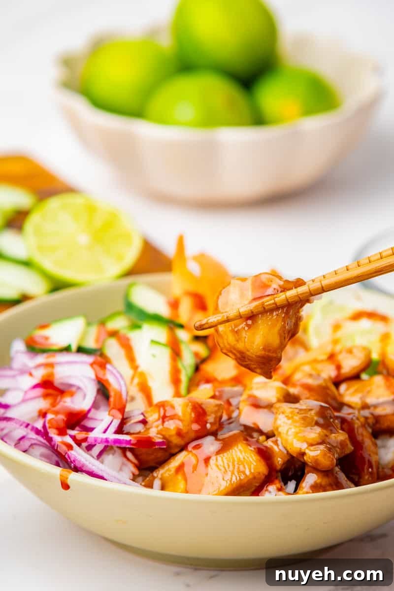 a poke bowl with teriyaki chicken, sliced cucumbers, red onion, and carrots with rice.