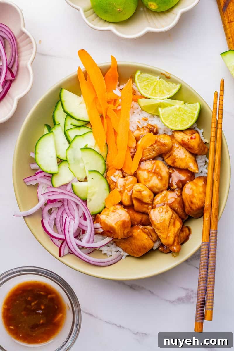 a chicken poke bowl with teriyaki chicken, cucumbers, carrots, red onion, lime slices, and white rice.