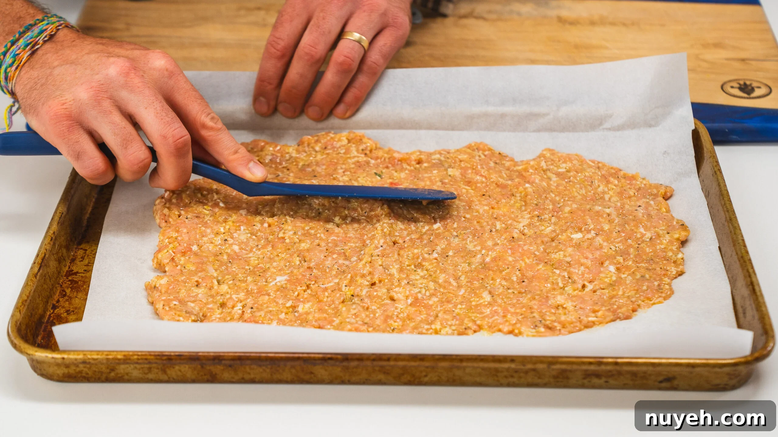 Chicken crust pizza being spread on a baking sheet with a spatula.