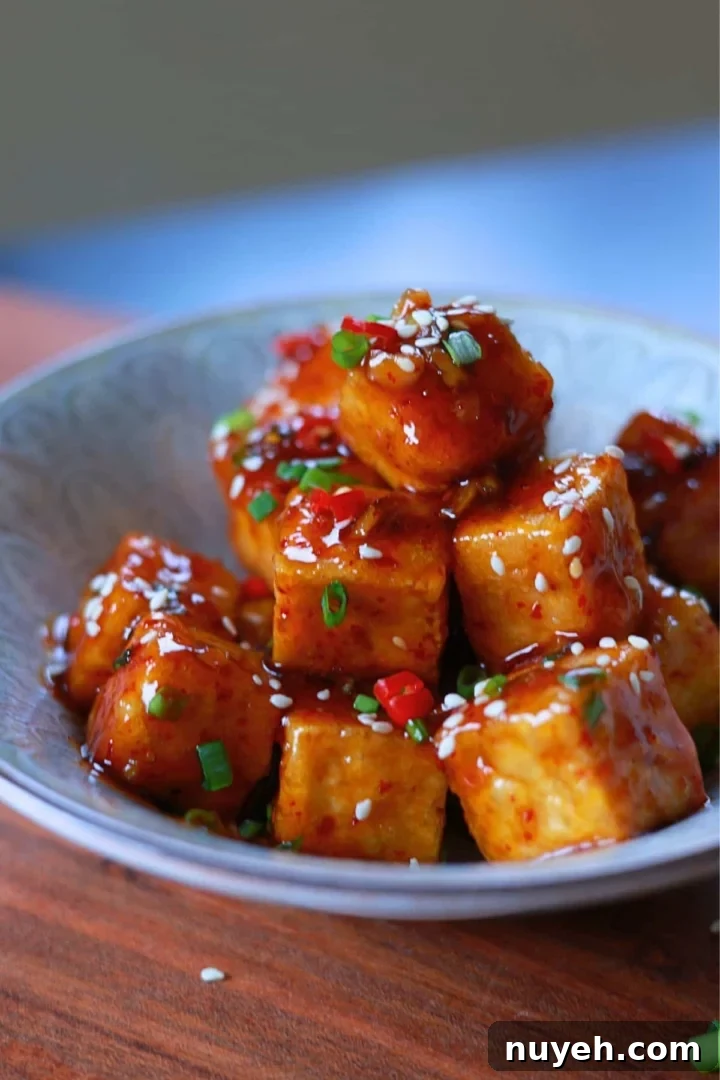 Sweet and Spicy Honey Garlic Tofu Recipe 2 A bowl of honey garlic tofu with a glossy, flavorful sauce, garnished with sesame seeds and green onions.
