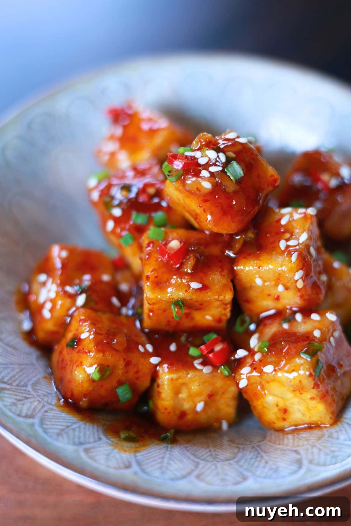 Sweet and Spicy Honey Garlic Tofu Recipe 6 A bowl crispy tofu cubes coated in a flavorful honey garlic glaze, topped with sesame seeds and green onions.