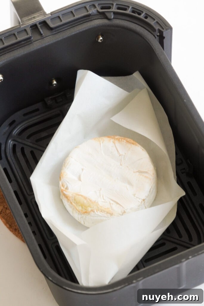 Air Fryer Baked Brie with Honey and Thyme 6 baked brie cheese in the air fryer basket after baking; the edges of the rind are slightly golden.