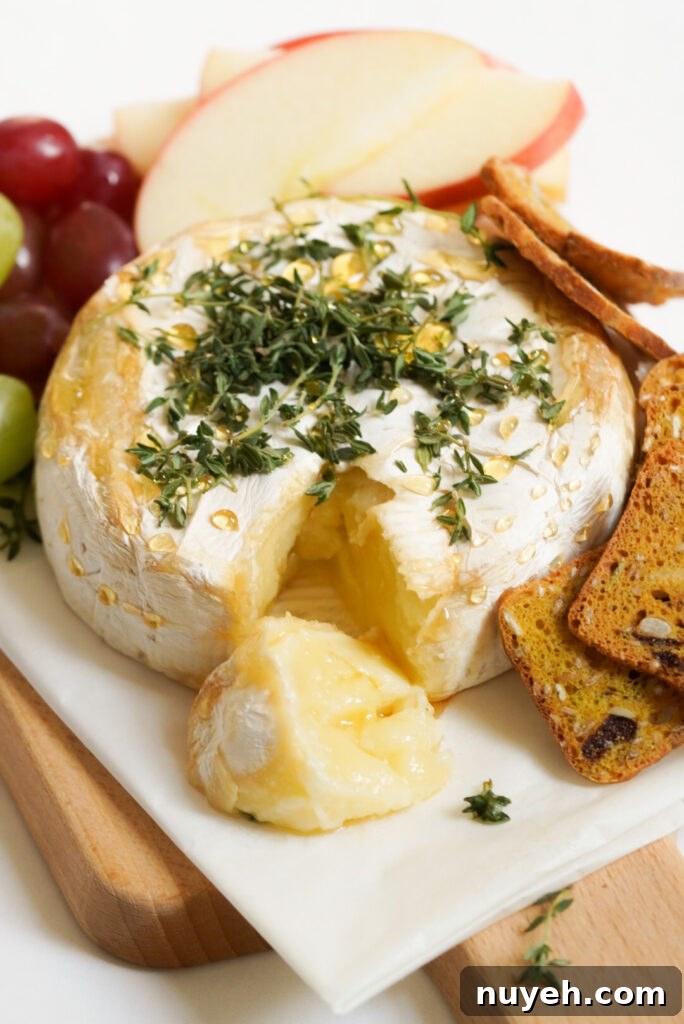 Air Fryer Baked Brie with Honey and Thyme 9 air fryer baked brie drizzled with honey and sprinkled with fresh thyme on a rectangular white serving platter with fresh fruit and crackers.