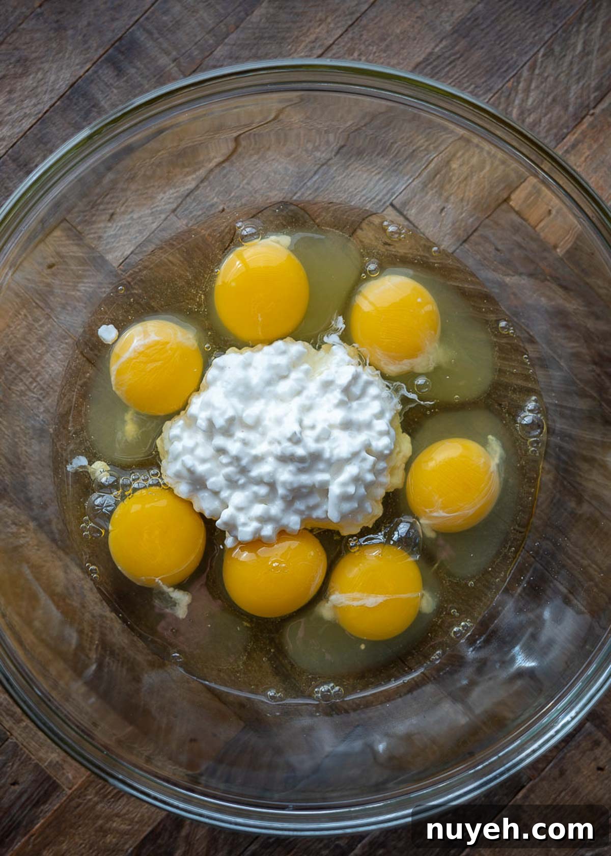 A mixing bowl with seven eggs and some cottage cheese in it