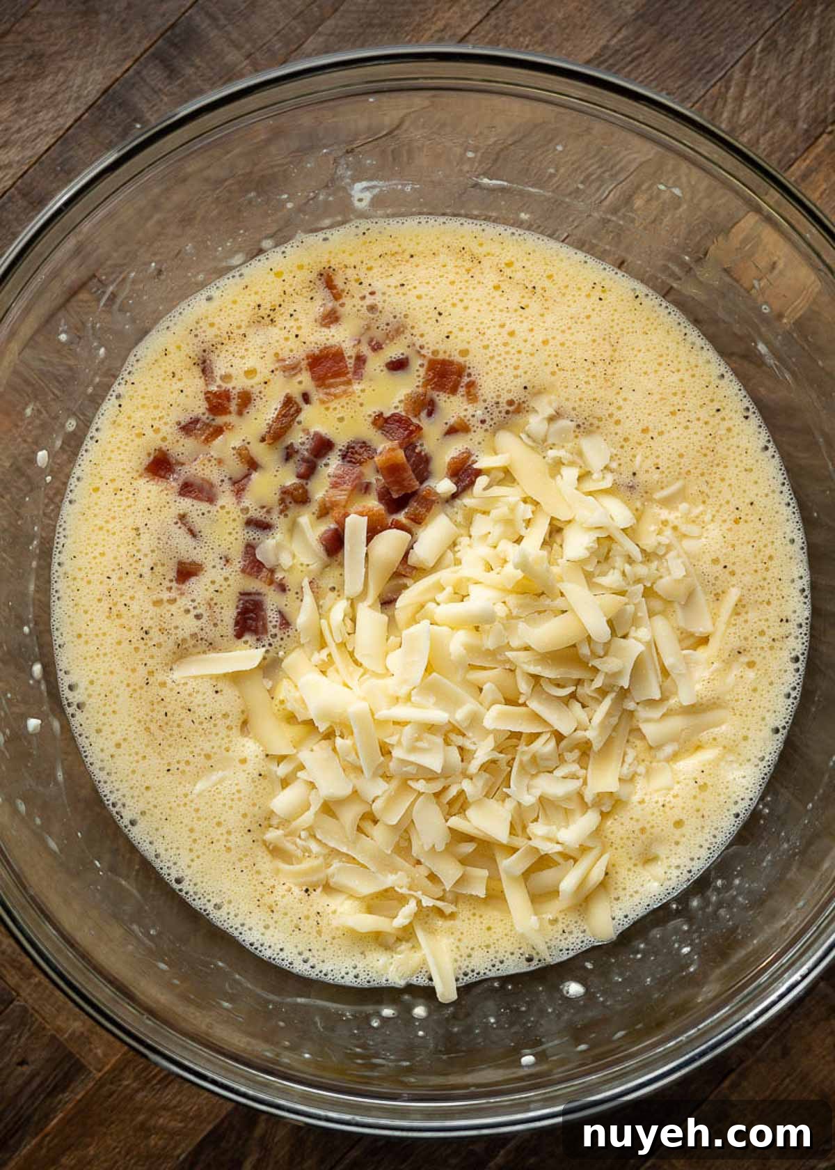 A mixing bowl with pieces of bacon and shredded cheese on top of a mixture of eggs and cottage cheese