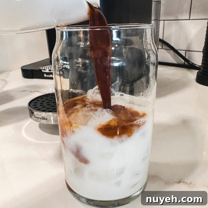 Slowly pour the brewed Nespresso Bianco Doppio coffee over the ice and milk, filling the glass about two-thirds full.