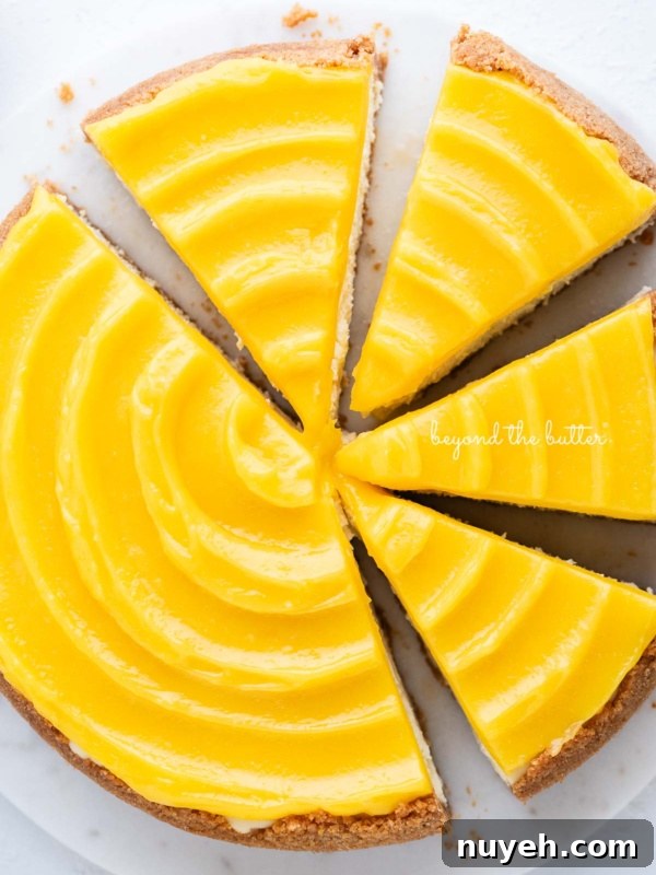 Lemon cheesecake topped with lemon curd cut into slices on a marble cake plate with white background.