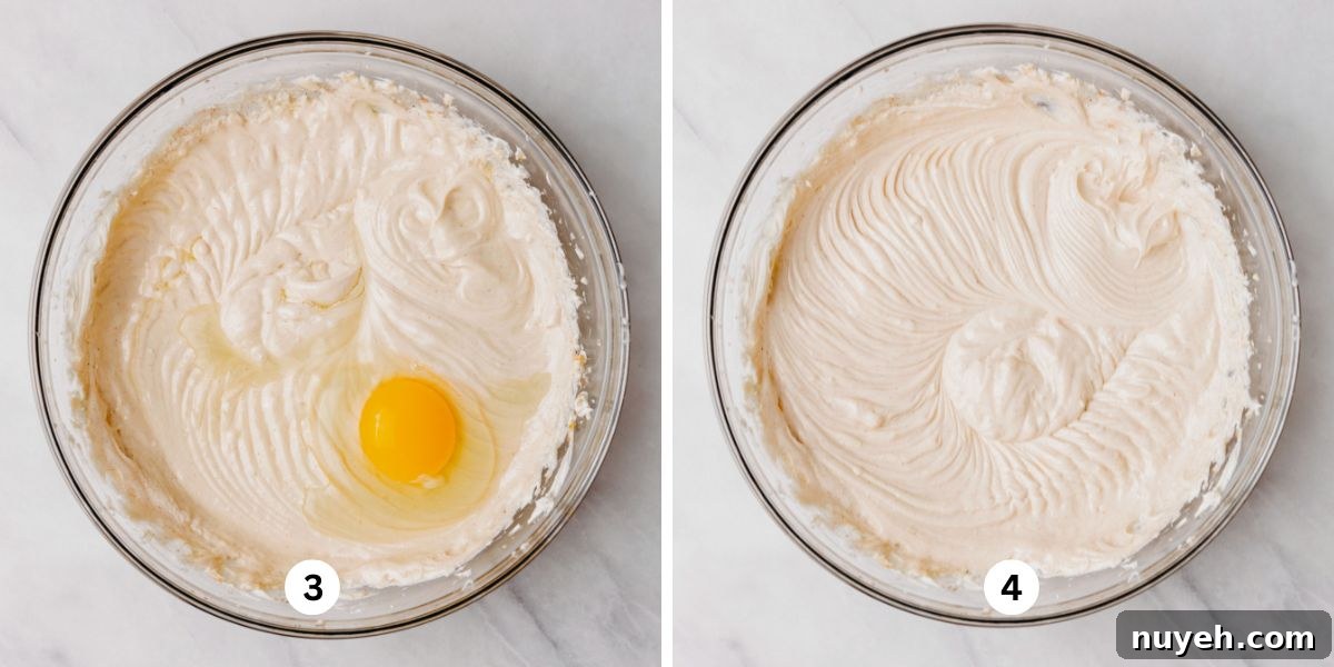 Adding eggs to cheesecake batter in a glass mixing bowl, mixing until each one is fully combined.