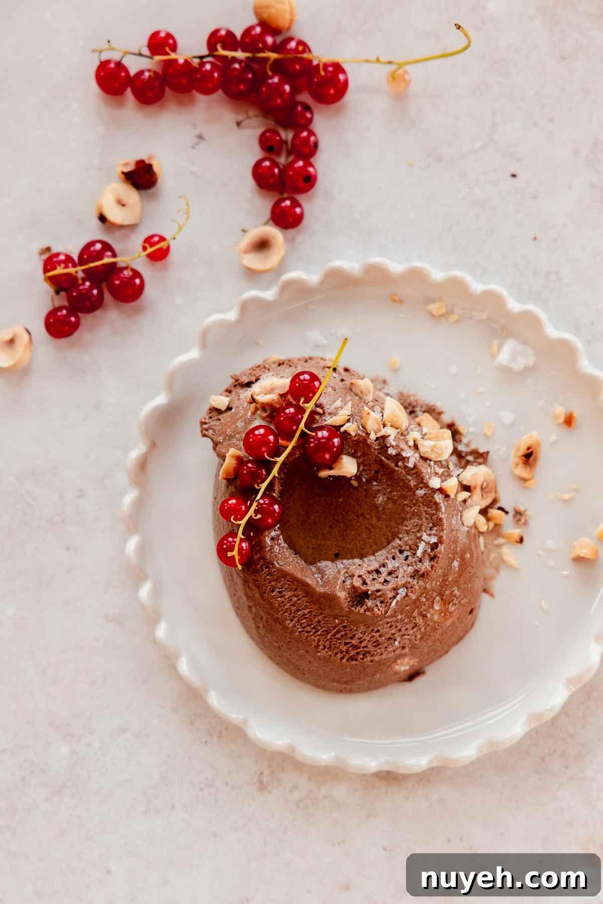 scoop of chocolate hazelnut mousse on a plate with chopped hazelnuts, red currant berries, and oil