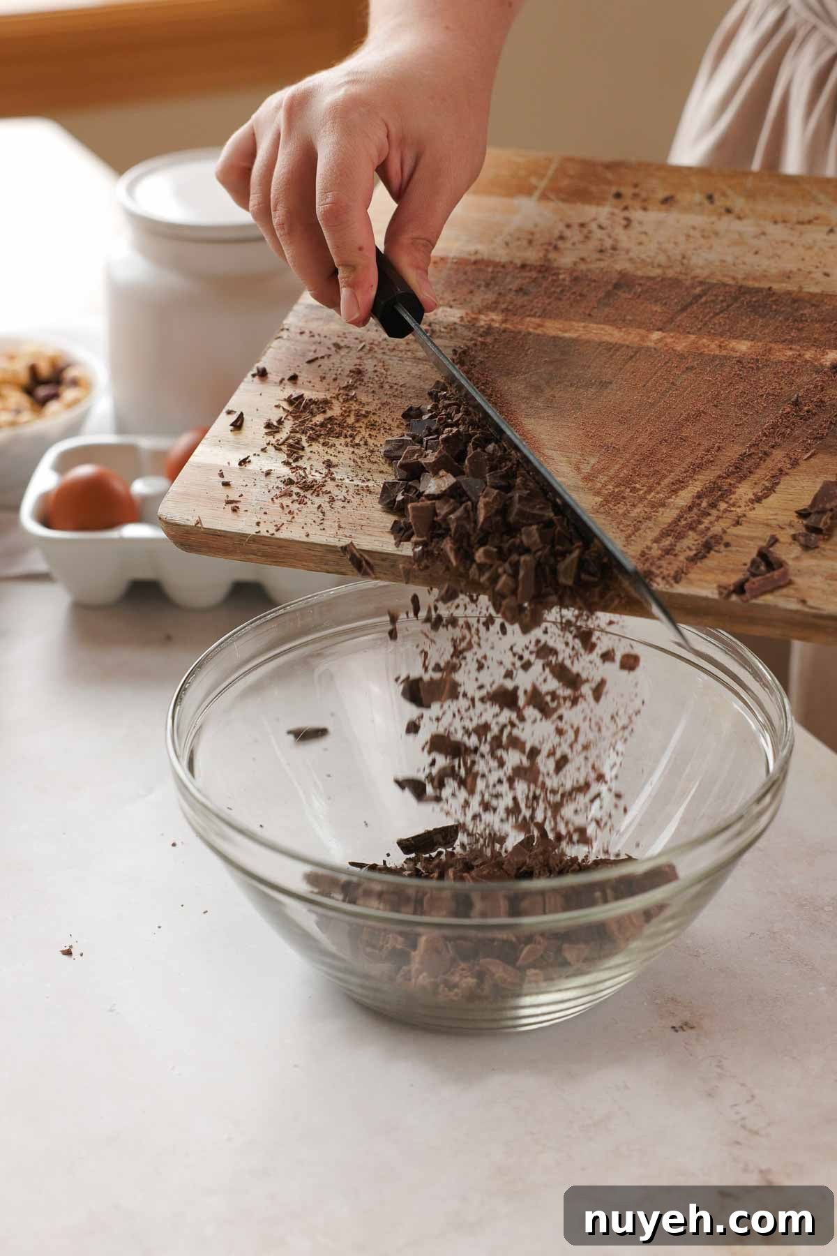 transferring chopped chocolate from a cutting board into a large glass bowl