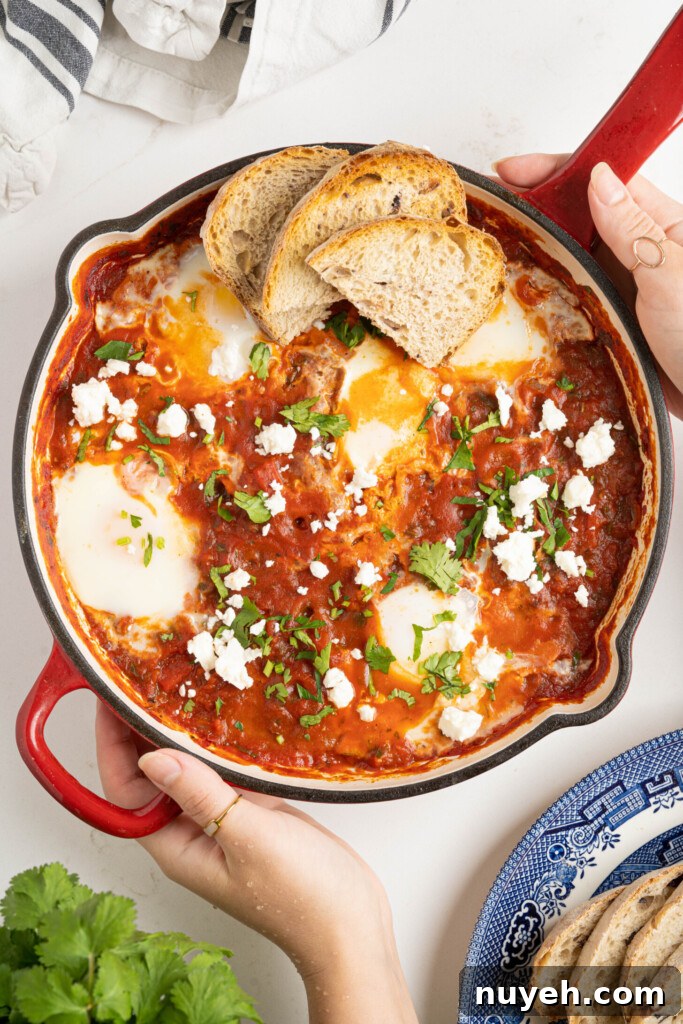 two hands holding shakshuka in a pan on a white counter