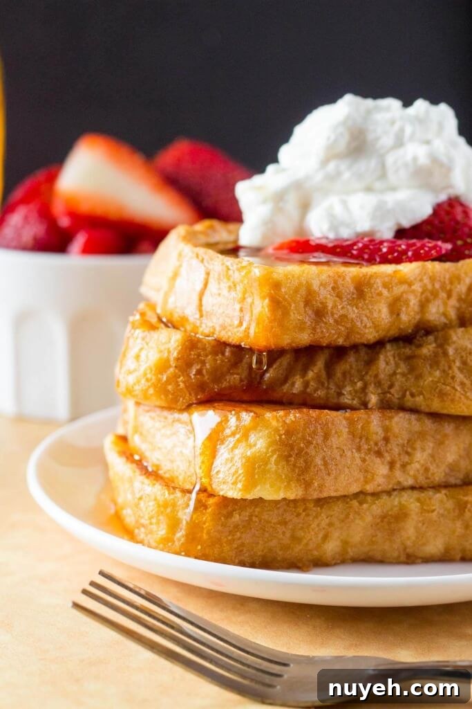 A tall stack for french toast topped with whipped cream and strawberries, then drizzled in maple syrup.