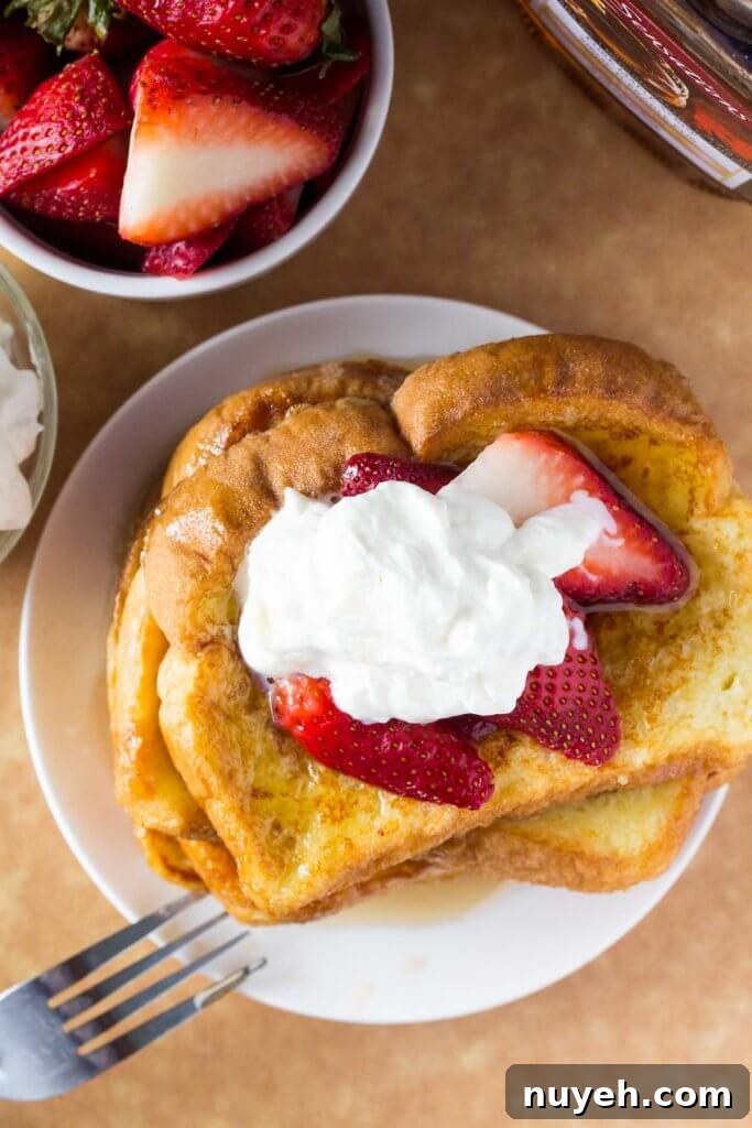Overhead shot of a stack of french toast with a bowl of strawberries and bottle of maple syrup.