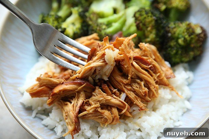 Shredded garlic honey chicken served over rice with a fork inserted diagonally on the left and a serving of steamed broccoli all on a plate.