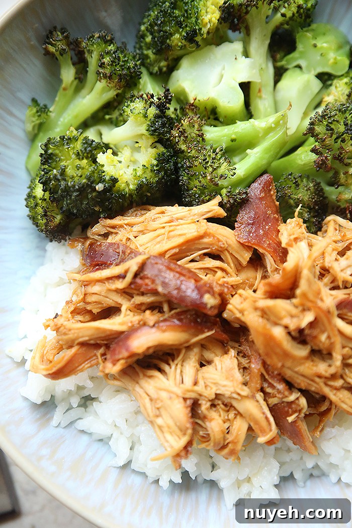 A serving of cooked broccoli and shredded honey garlic chicken over rice on a light blue dinner plate.