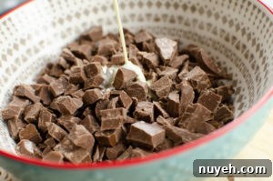 Hot cream being poured onto milk chocolate chunks in a blue and white bowl
