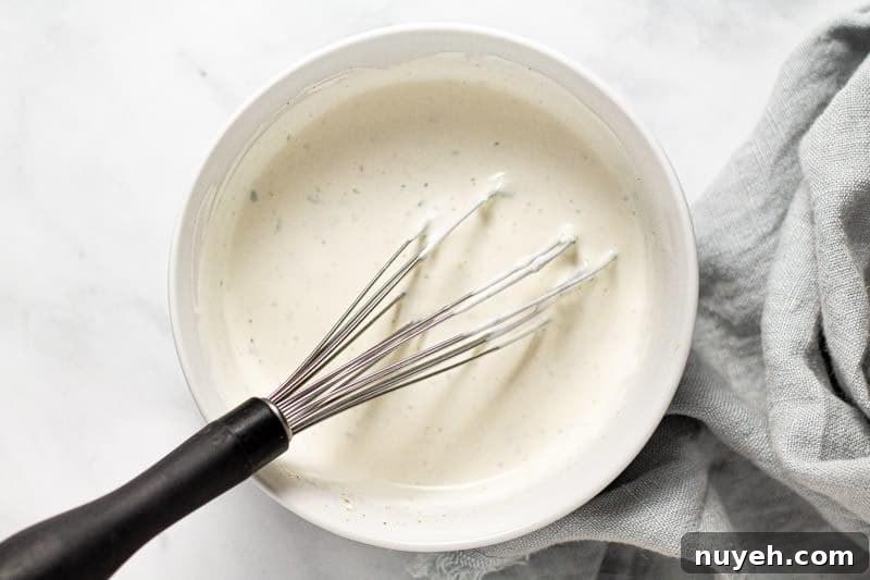 Overhead shot of a white bowl filled with ingredients to make Mexican street corn flatbread sauce
