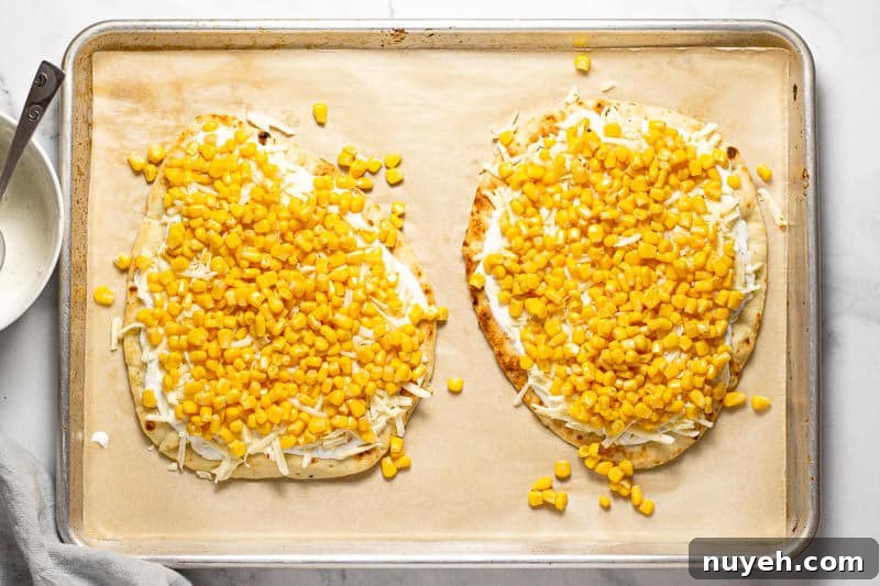 Large baking sheet with two Mexican street corn flatbreads with creamy sauce and corn on them