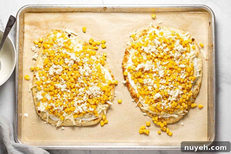 Large baking sheet with two Mexican street corn flatbreads with creamy sauce and corn on them