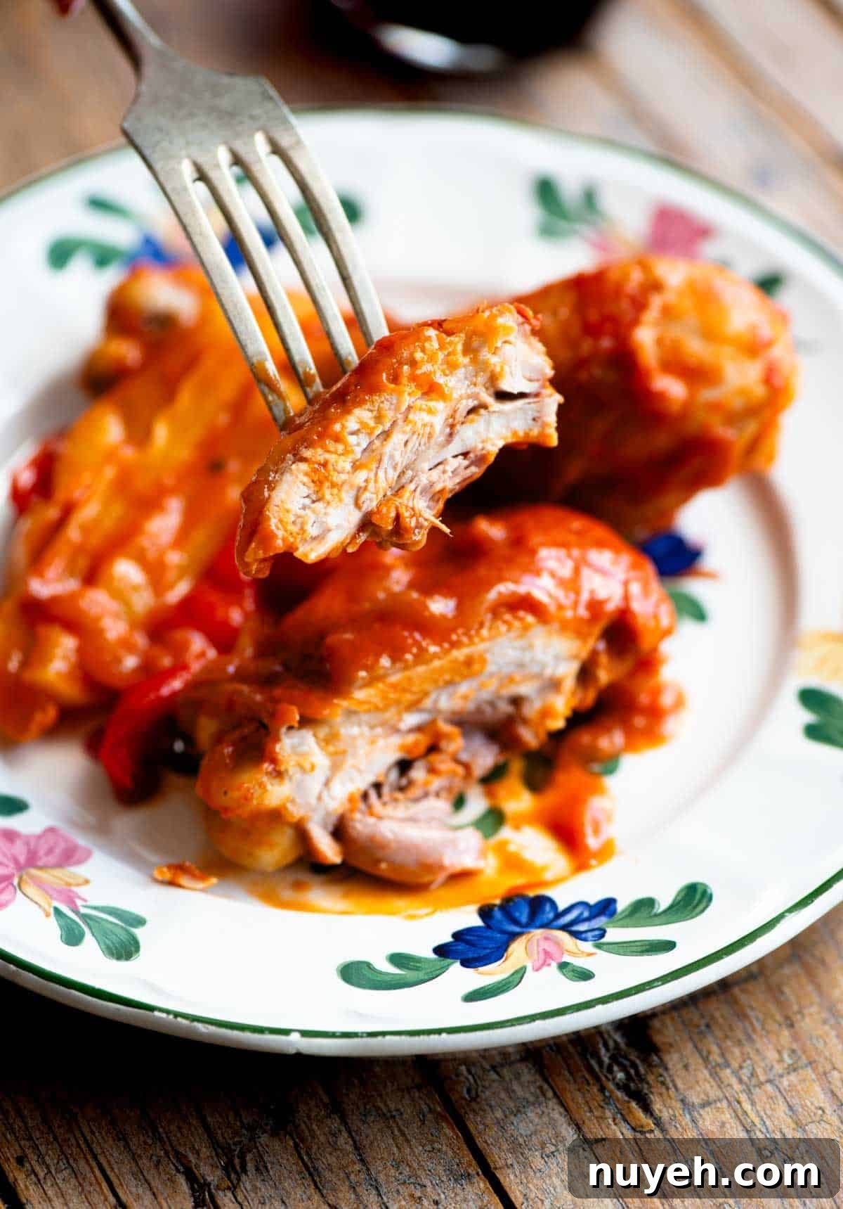 A close up of a piece of chicken on a fork covered in tomato sauce.