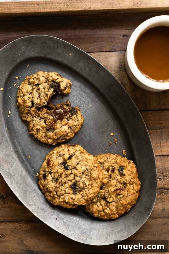 Three oatmeal cookies on an oval plate next to a cup of coffee.