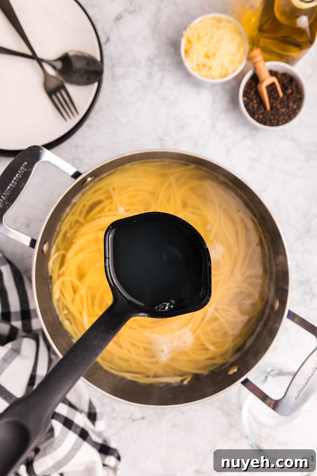 A ladle lifts starchy pasta water from a pot of cooking spaghetti, a key step in preparing pasta alla Nerano, on a kitchen counter.