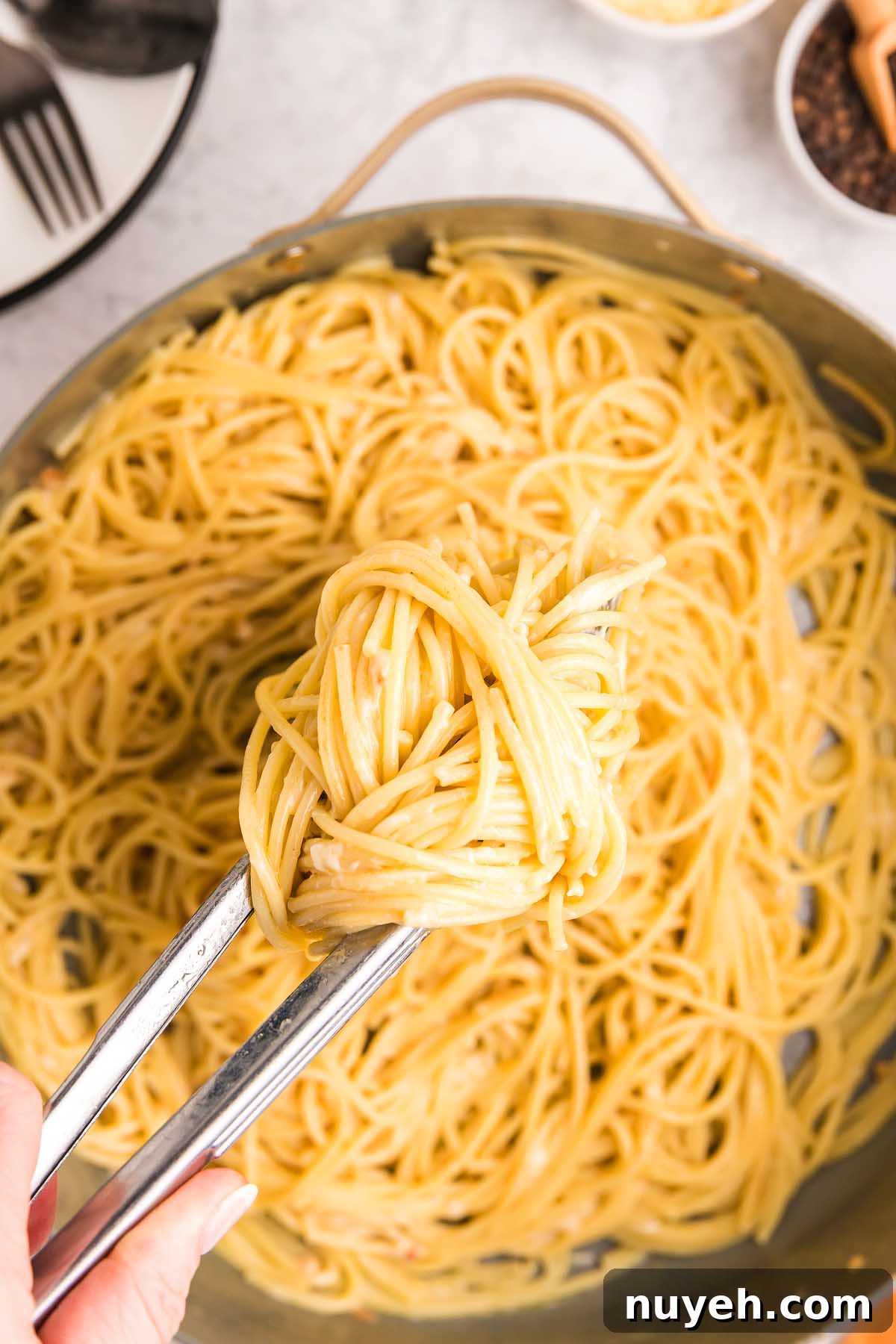 Tongs holding a portion of pasta alla Nerano above a pan filled with more spaghetti.