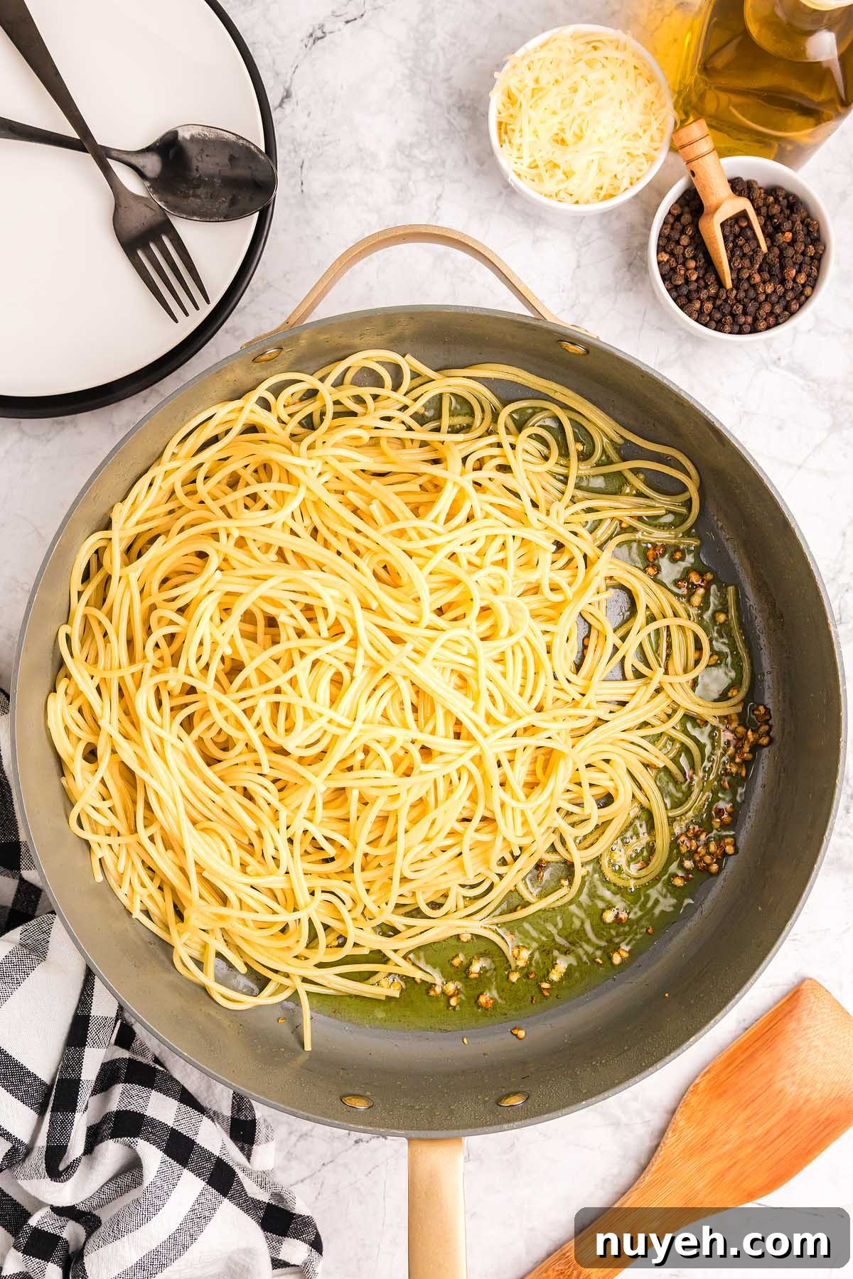 Cooked spaghetti pasta alla Nerano in a large skillet with olive oil, pepper, cheese, and utensils on a marble countertop.