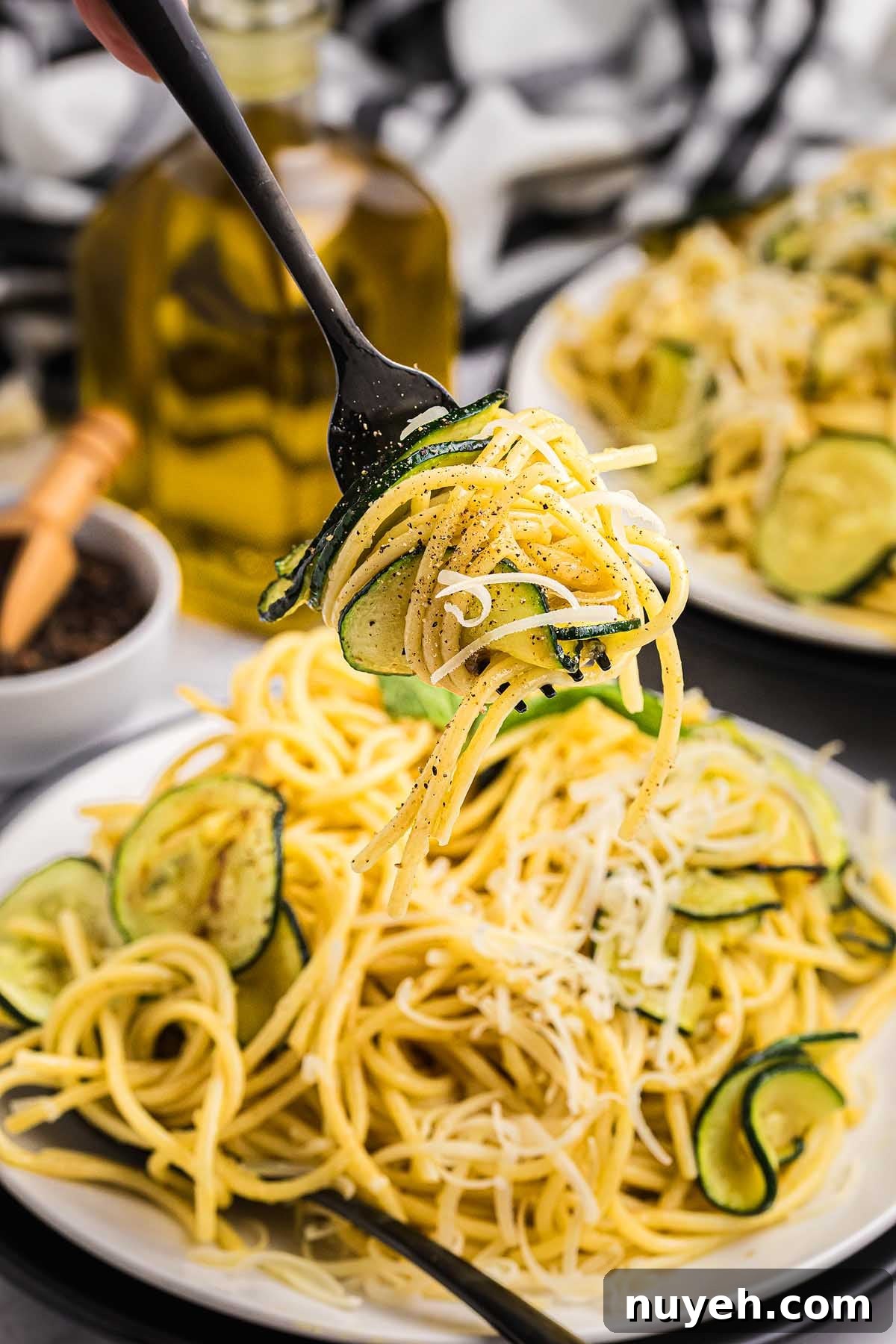Fork lifting spaghetti with zucchini, black pepper, and grated cheese above a plate of pasta alla Nerano.