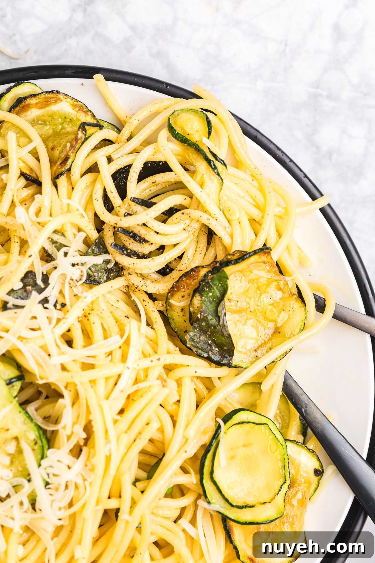 Spaghetti pasta alla Nerano with sautéed zucchini slices, grated cheese, and black pepper on a white plate.