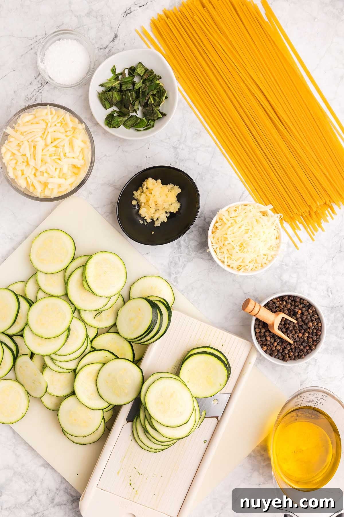 Sliced zucchini, dry spaghetti, cheese, basil, garlic, oil, salt, and pepper arranged on a marble countertop—perfect ingredients for pasta alla Nerano.