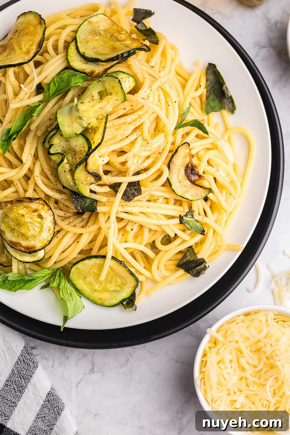 Plate of pasta alla Nerano featuring sautéed zucchini and fresh basil, served alongside a bowl of shredded cheese.