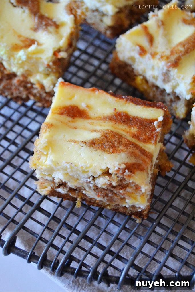 Carrot Cake Cheesecake Bars with Cream Cheese Frosting Recipe 2 an aerial shot of a carrot cake cheesecake bar sitting on a black cooling back.