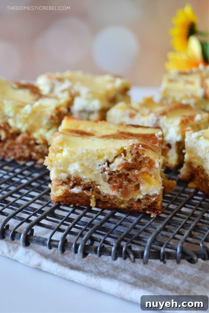 Carrot Cake Cheesecake Bars with Cream Cheese Frosting Recipe 3 an arrangement of carrot cake cheesecake bars on a black wire rack sits against a light spotted background. some yellow flowers are off to the right in the background.