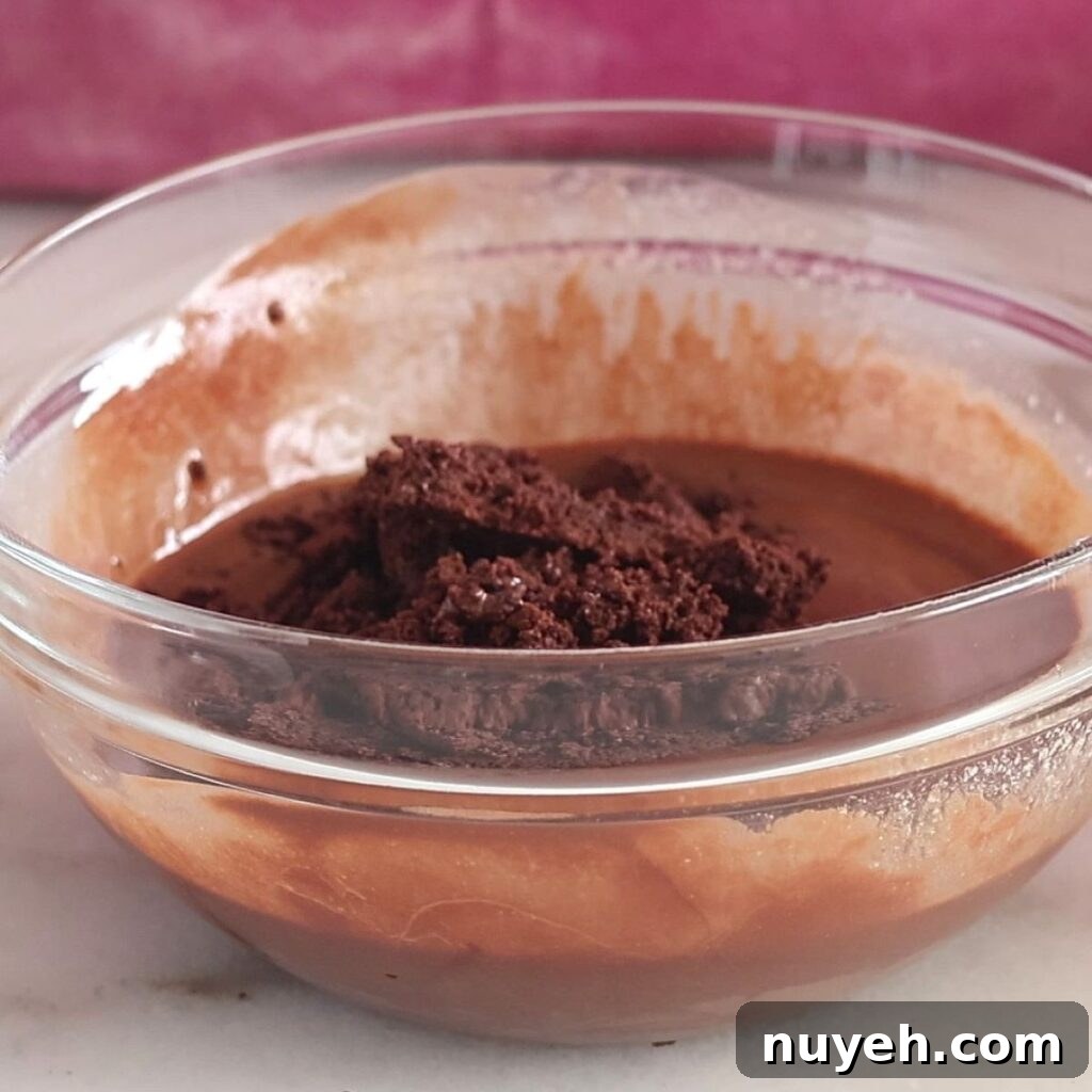 adding chocolate cookie crumbs to glass bowl of melted chocolate.