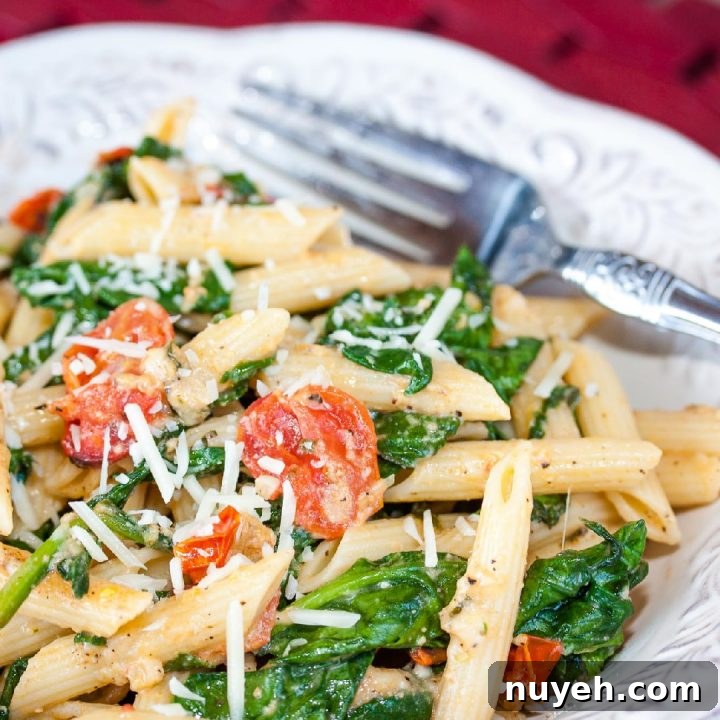 White plate with penne pasta, cooked baby spinach, cherry tomatoes, and shredded mozzarella cheese