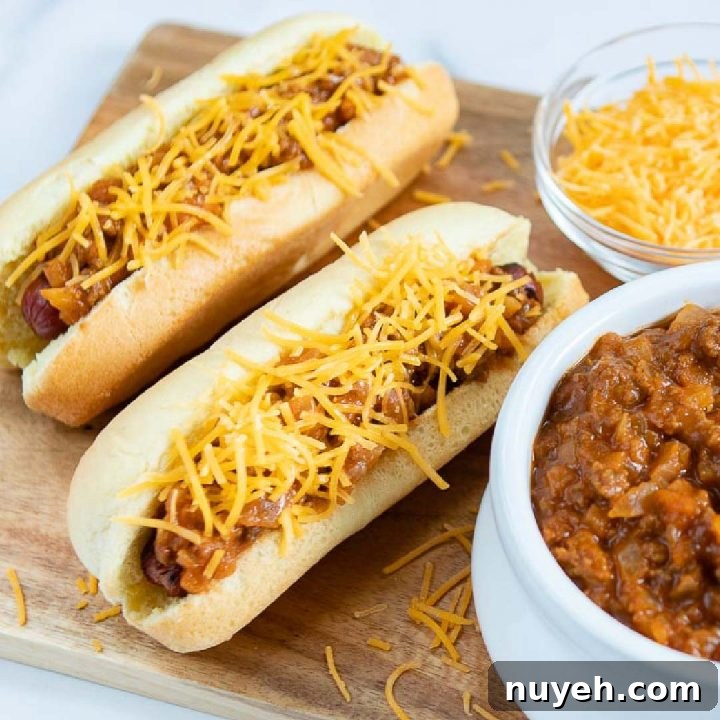 Two hot dogs in buns topped with chili and shredded cheese, a bowl of shredded cheese, and a bowl of chili