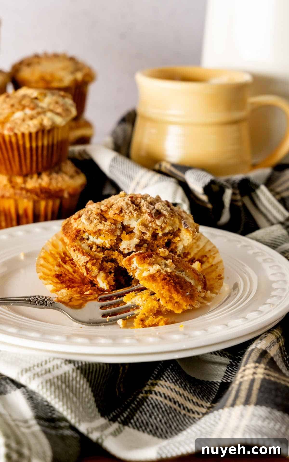 Pumpkin cream cheese muffin cut open with a fork on a white decorative plate.