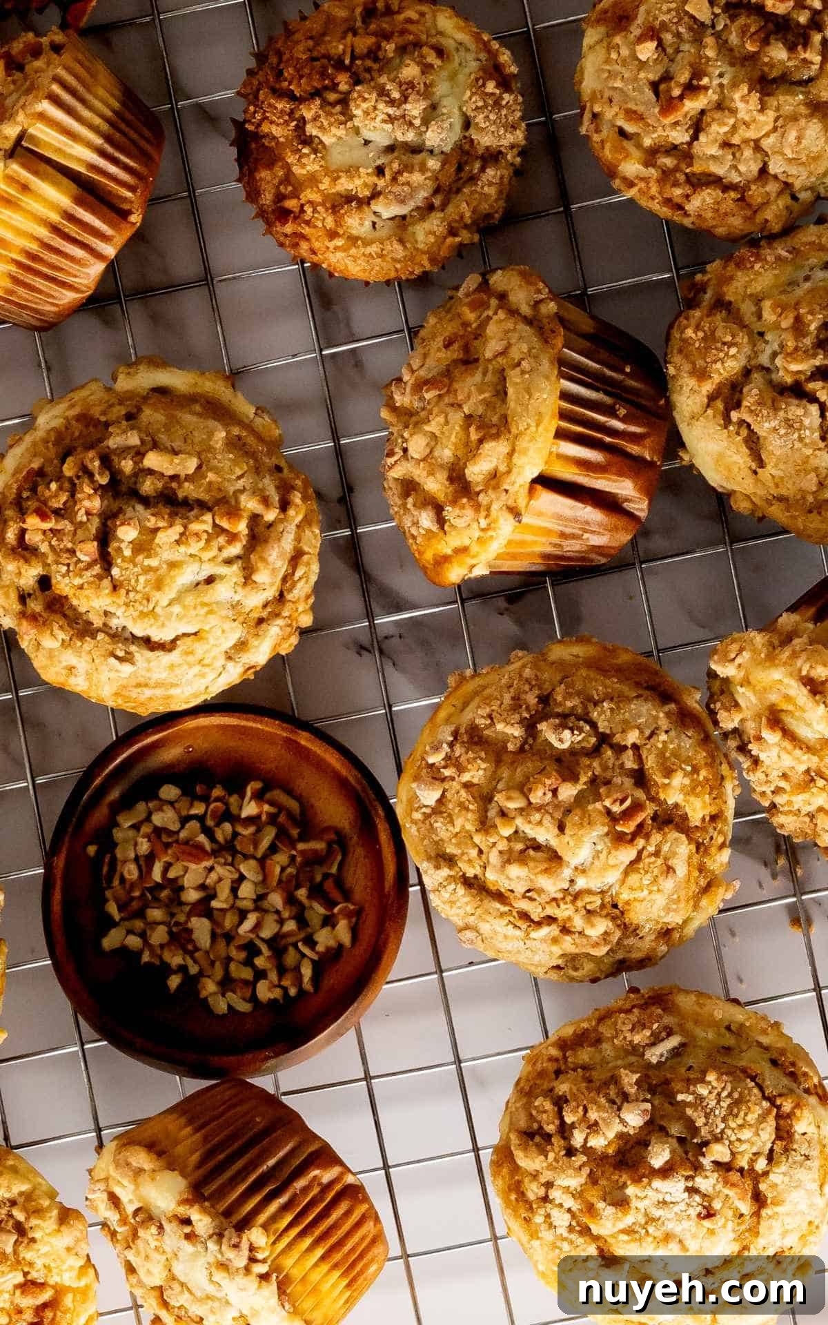 Pumpkin cream cheese muffins cooling on wire rack with a bowl of chopped pecans.