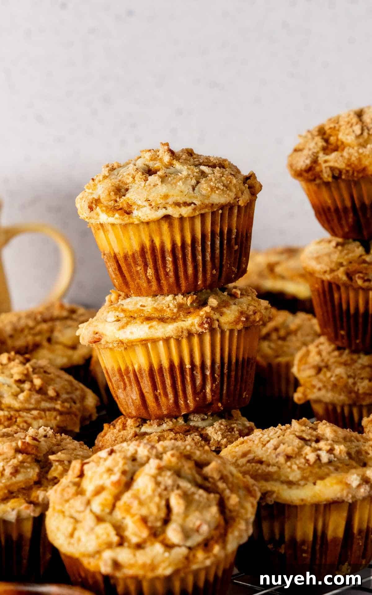 Three pumpkin cheesecake muffins stacked on linen with muffins surrounding it.