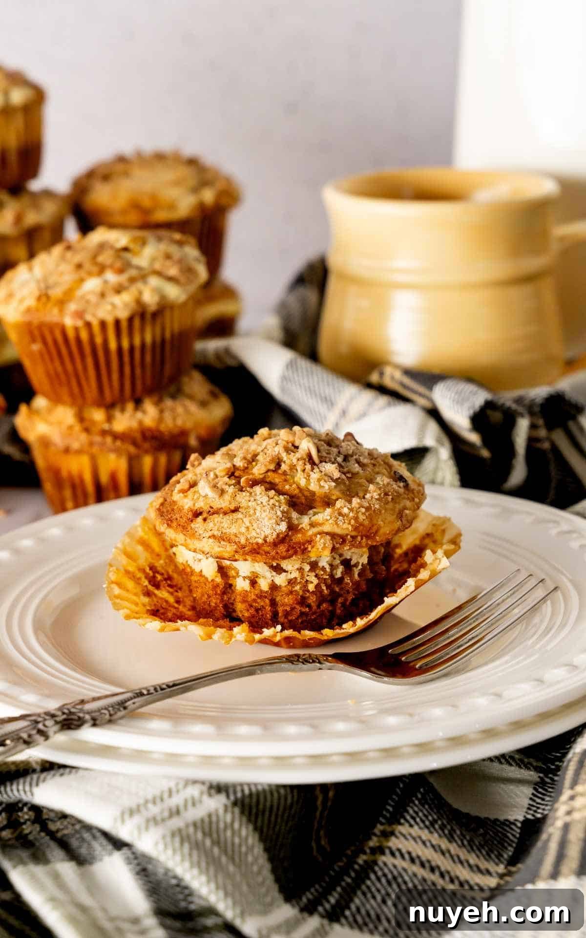 A pumpkin cheesecake muffin with the wrapper peeled back sitting on a white decorative plate with a fork.