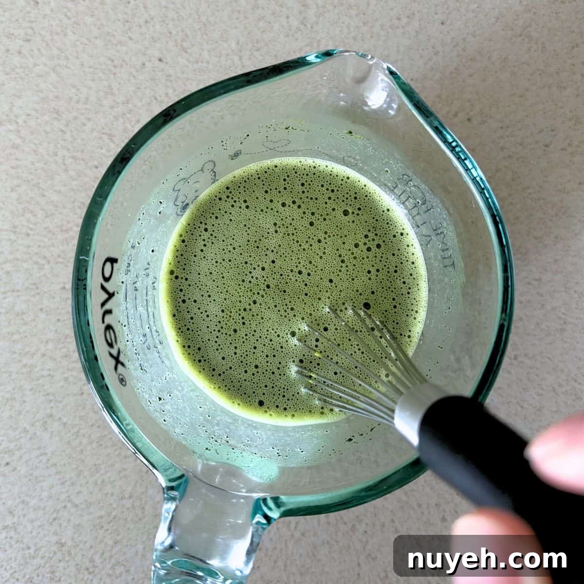 Whisking matcha powder and sugar into warm milk.