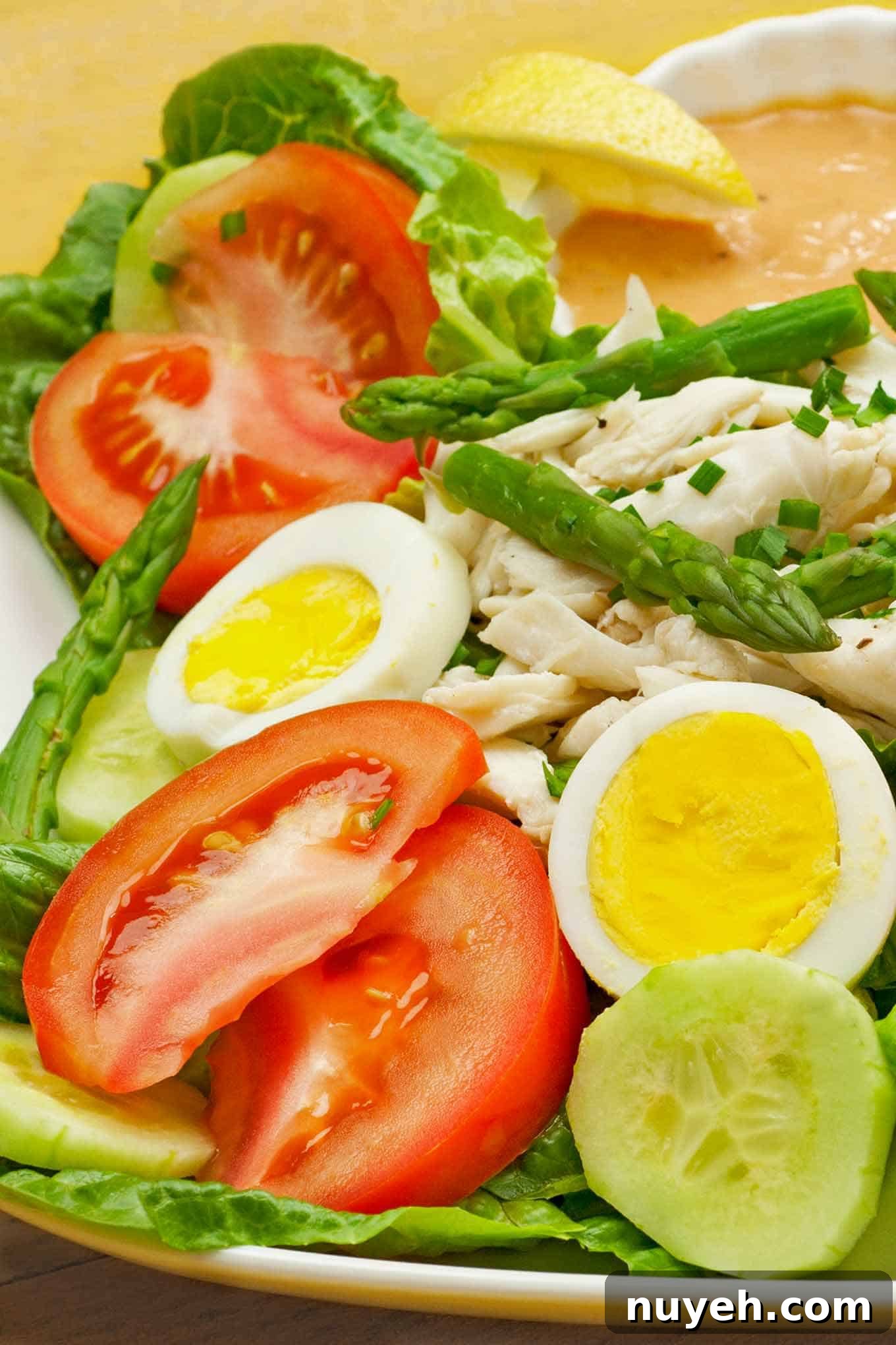 Crab Louie salad on a plate, lettuce, tomato, cucumber, hard cooked eggs, asparagus, lump crab meat, dressing, and a lemon wedge.
