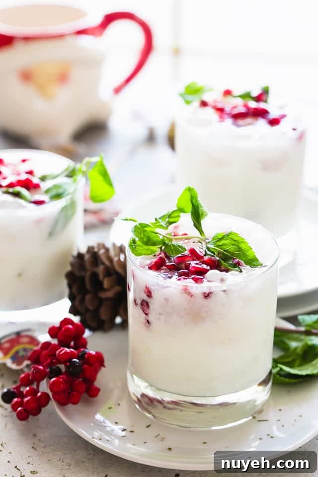 Coconut mojitos served in a whisky glass and garnished with pomegranate seeds and fresh mint leaves.