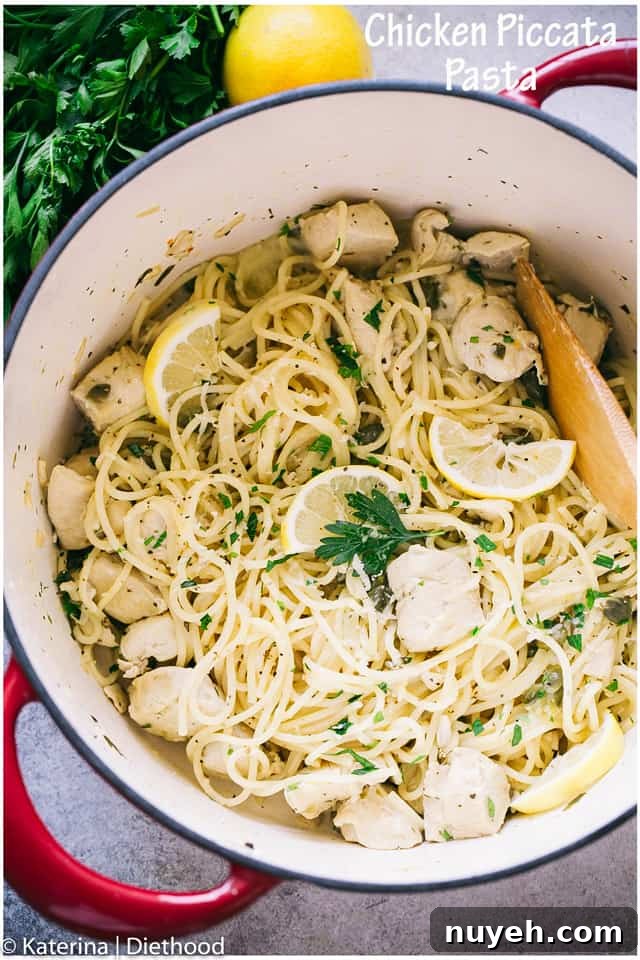 Chicken piccata pasta in a pot beside a lemon and a sprig of fresh parsley