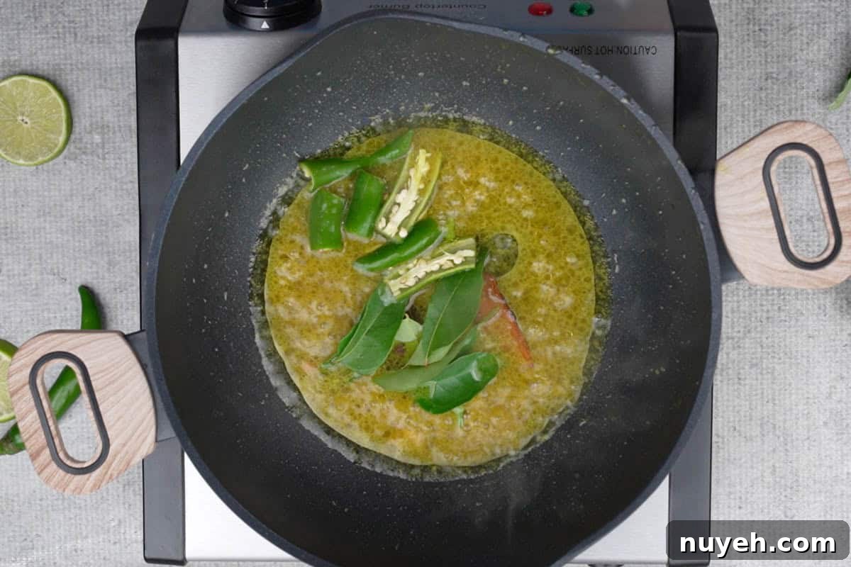 Whole spices, curry leaves and green chilies added to the pan.