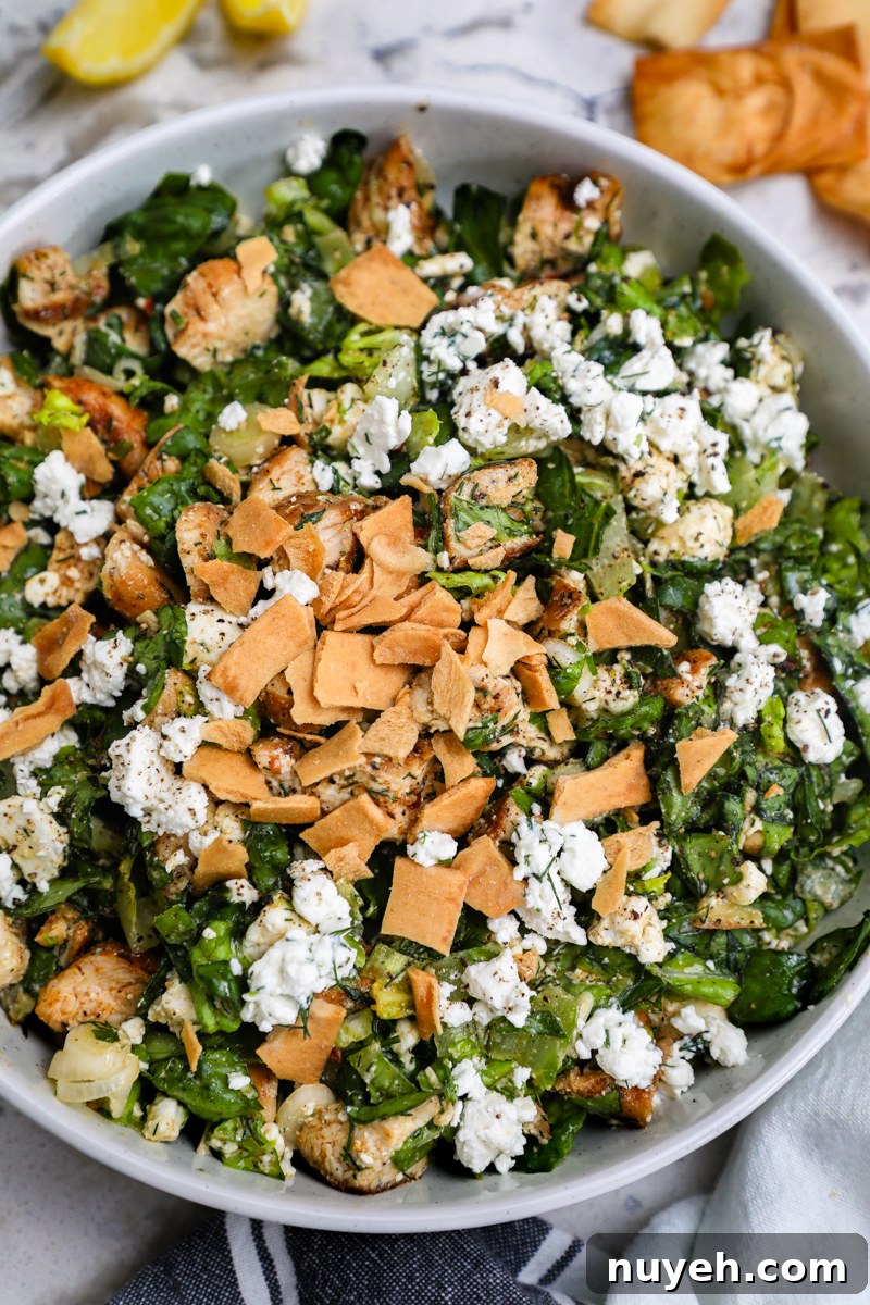 Crisp Chopped Chicken Salad with Feta and Lemon Vinaigrette 2 A white serving bowl filled with chopped chicken feta salad garnished with crushed pita chips sitting on a marble countertop