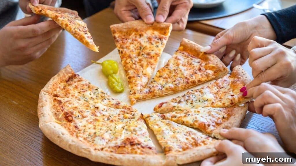 Several people take slices of cheese pizza from a shared pizza on a wooden table, with two yellow peppers on the pizza—celebrating National Cheese Pizza Day together.