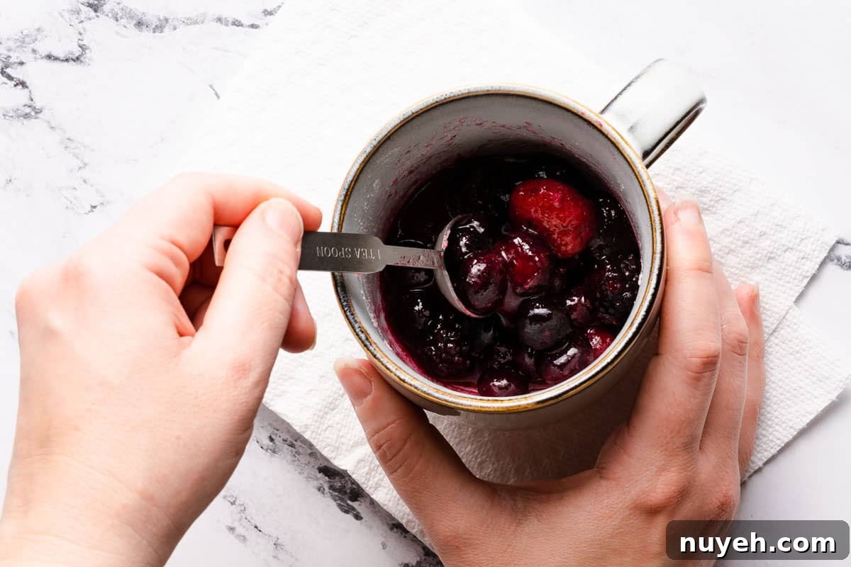 spoon mixing microwaved berries in mug